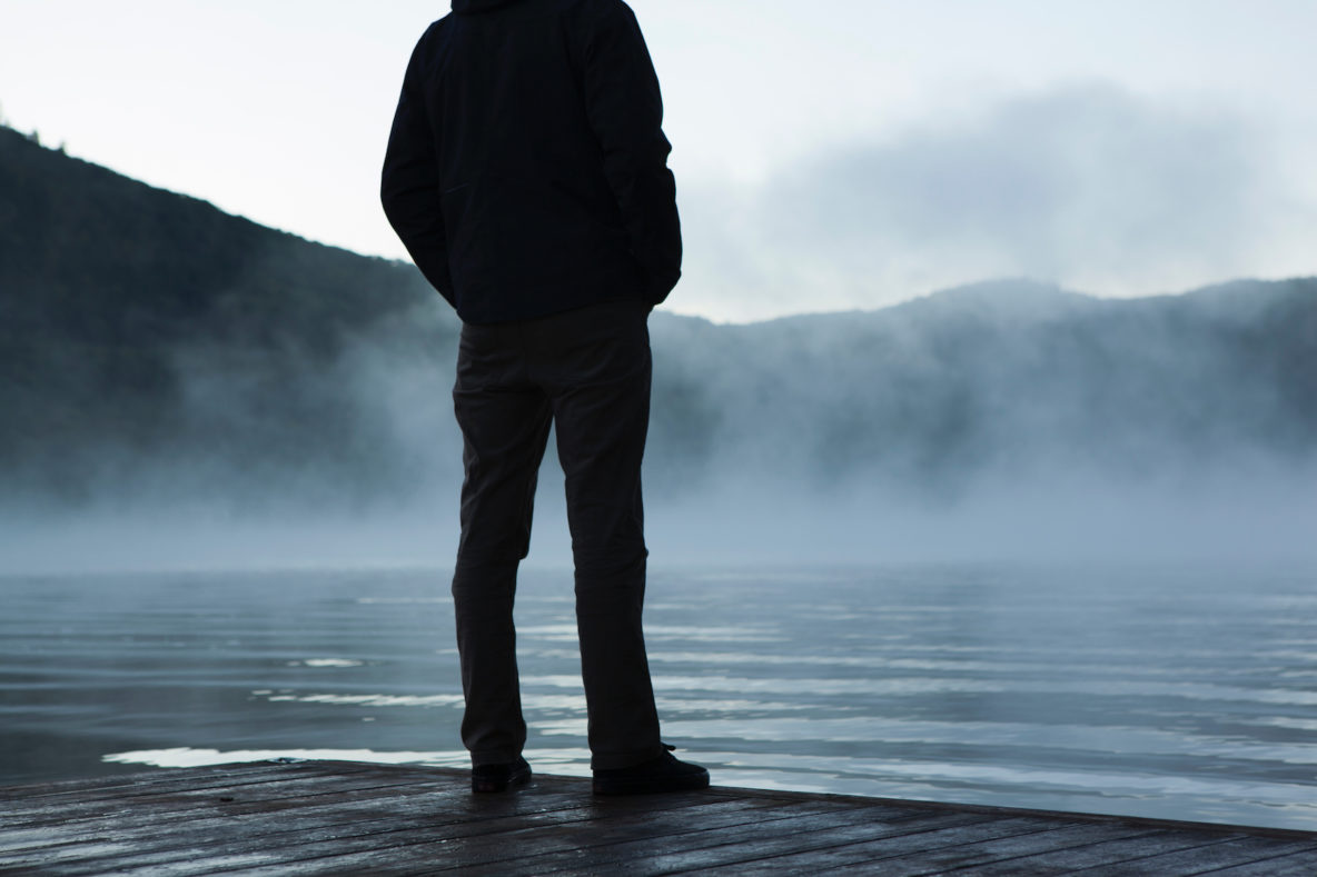 Man standing on dock at mountain lake.