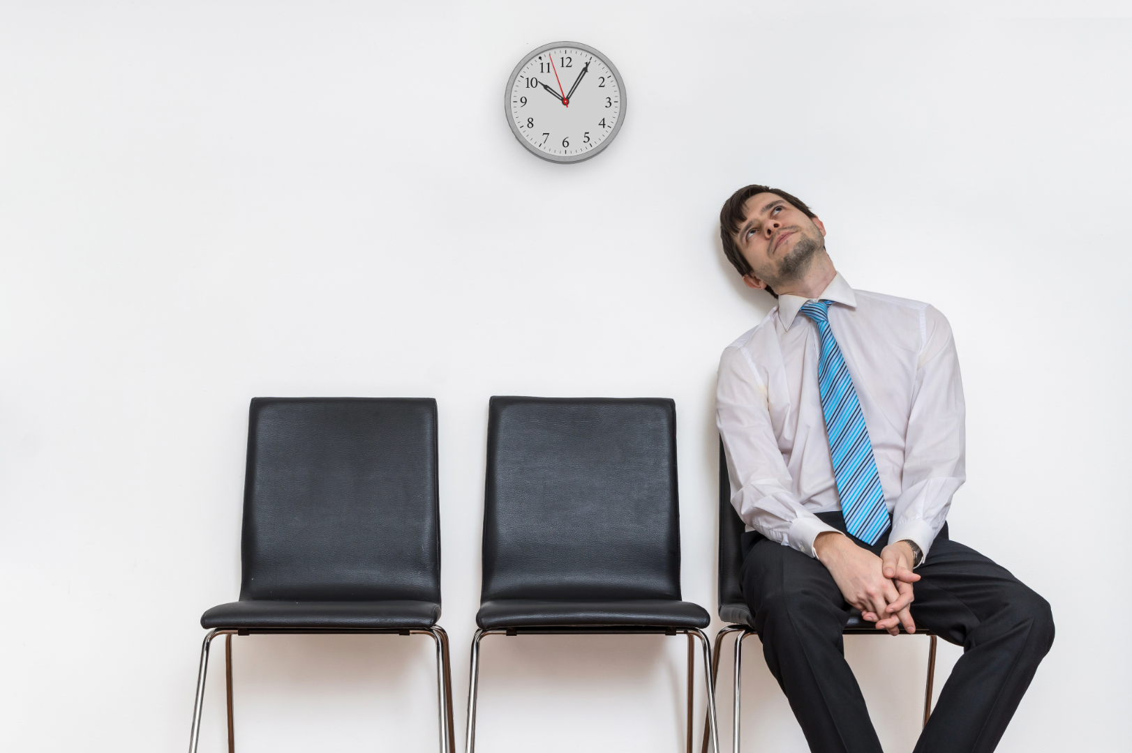 A Man Sitting Alone in a Waiting Room Looking Bored With a Clock on the Wall